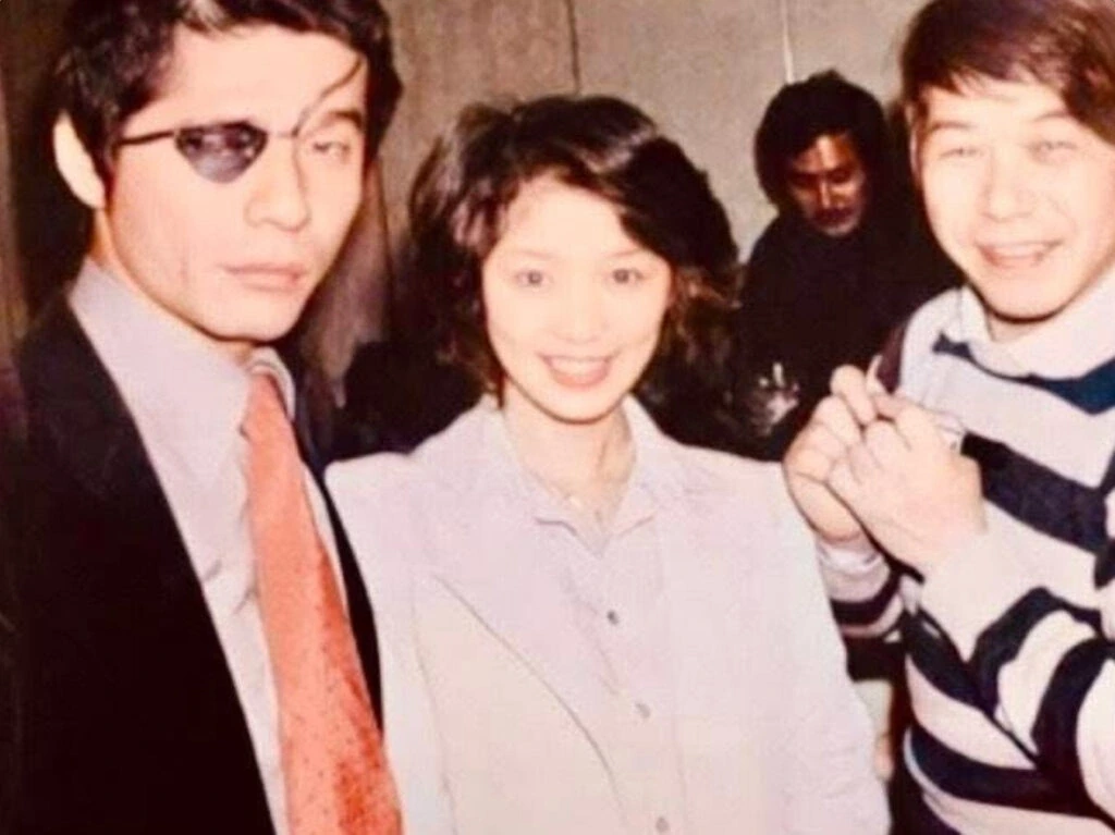 タモリさんが1970年代の仲間との集合写真で細めのメタルフレームサングラスを着用しているショット（左）