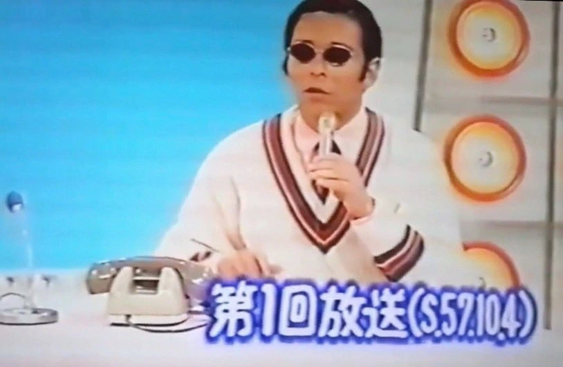 タモリさんが『笑っていいとも！』第1回放送でセーター姿にメタルフレームのサングラスを着用しているカット