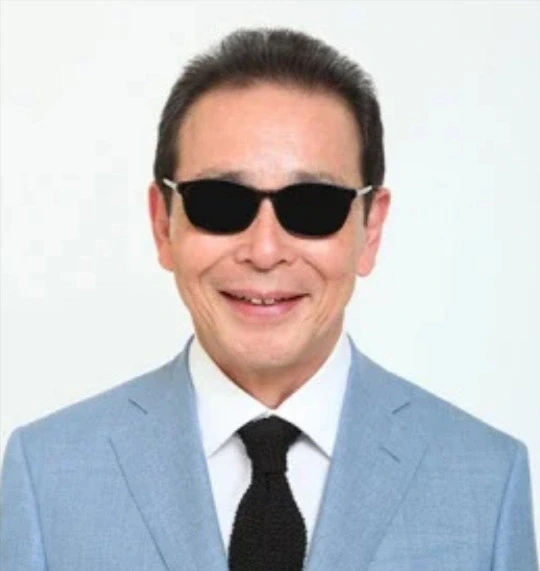 タモリさんが水色のジャケットに黒い樹脂のウェリントン型サングラスを着用した正面ポートレート