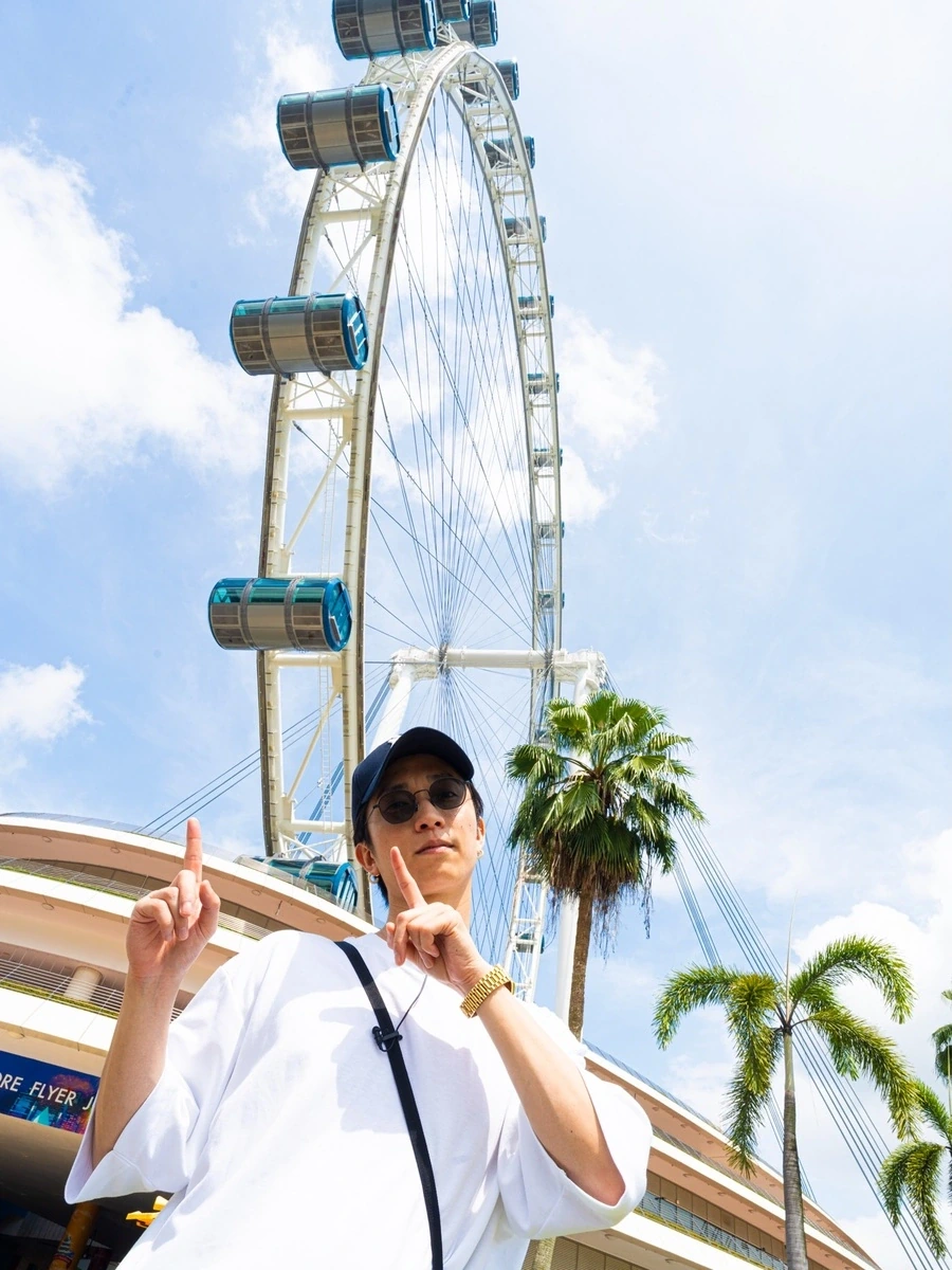 京本大我さんがシンガポール旅の私服で観覧車を背景にラウンド型のブラックサングラスを着用しピースサインをするショット
