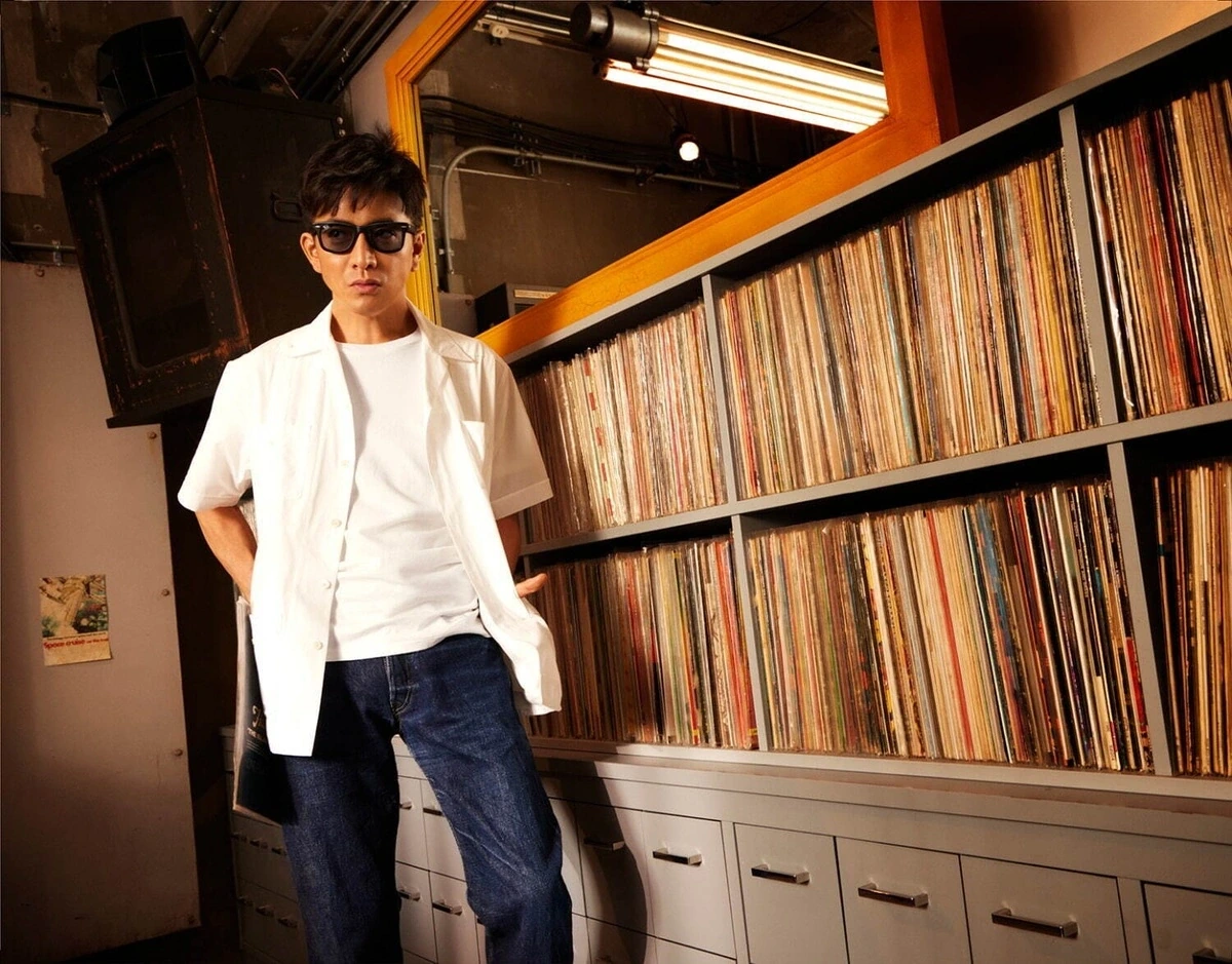 木村拓哉さんがRay-Banの公式キャンペーンでレコード店を背景に白シャツとデニムにブラックのウェイファーラー型サングラスを合わせた全身ショット