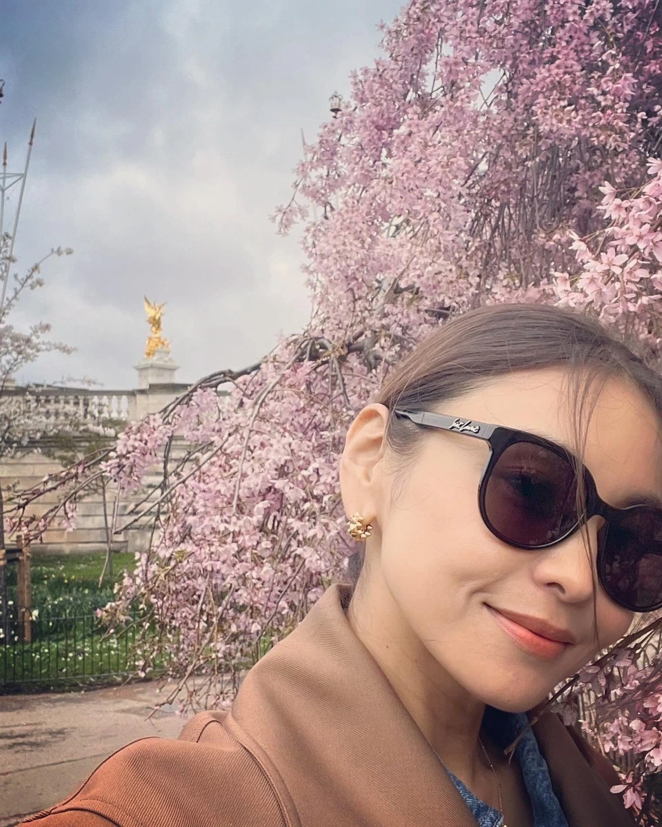 滝沢眞規子さんがロンドンの桜を背景にSAINT LAURENTの黒いラウンド型SL317Fを着用した自撮りショット
