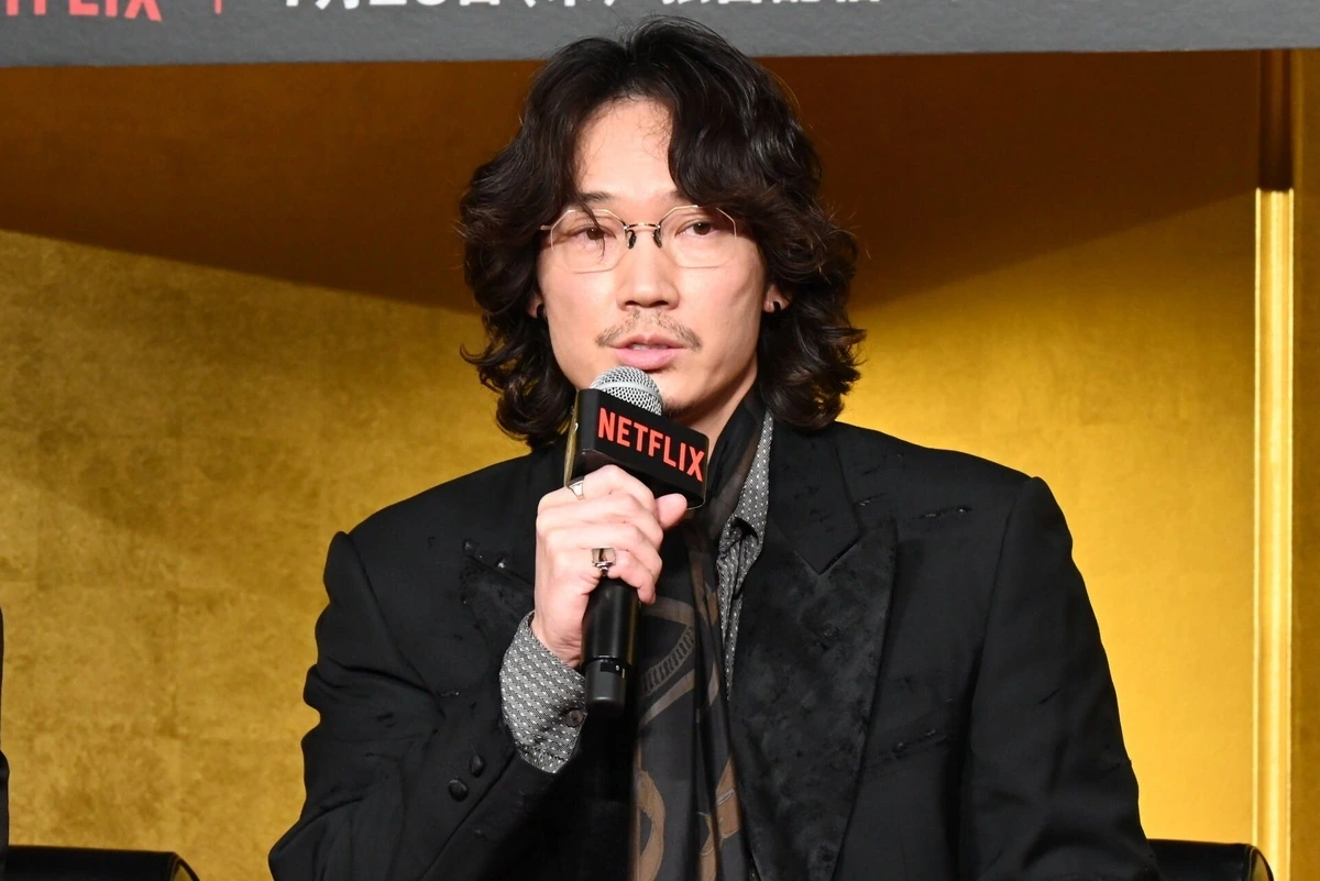 綾野剛さんがNetflix『地面師たち』の完成報告会見でマイクを手にクリアフレームのメガネを着用しているショット